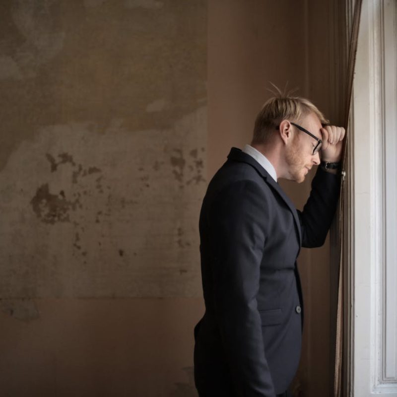 Mann der sich verzweifelt gegen das Fenster lehnt